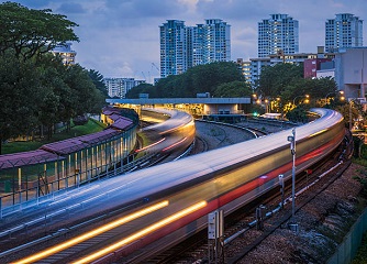 Mass Rapid Transit (MRT) trains arriving and leaving the station of Ang Mo Kio in Singapore. The image was taken in the evening during blue hour and the trains have motion blur